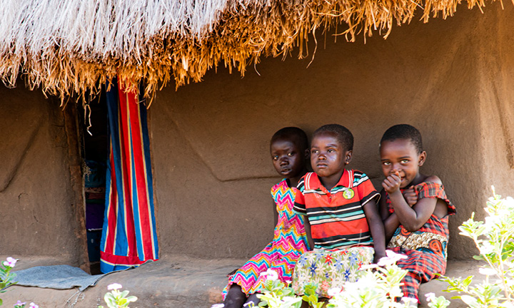 Kolme pientä ugandalaislasta istuu talon edessä.