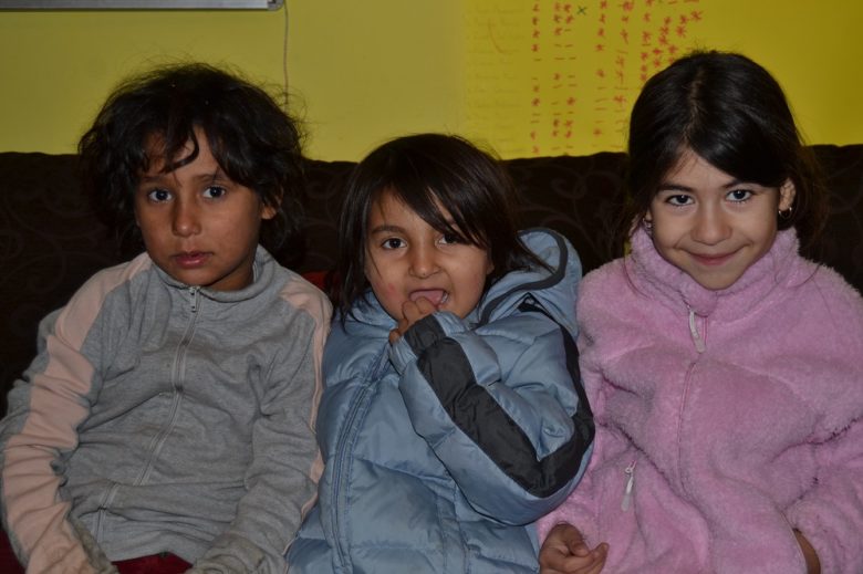 Kolme pientä romanityttöä istuu sohvalla takit päällä.