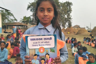 Nepalilainen koulutyttö koulupuvussa pitää kädessään värikästä oppikirjaa.