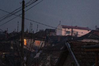 Kuvassa näkyy pimeässä hohtava ikkuna ja kirkon risti illan hämärässä slummissa Bulgariassa.