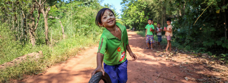 Kuvassa myanmarilainen pieni poika vierittää kumirengasta tiellä.