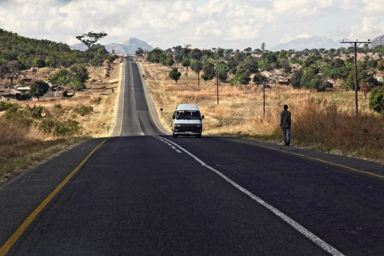Autotie Malawissa. Ihmisiä kävelee tien reunassa ja tiellä ajaa valkoinen pakettiauto.