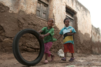 Kaksi pientä etiopialaista lasta leikkii kadulla vanhalla auton renkaalla.