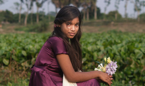 Violettipukuinen tyttö kukkakimpun kanssa.