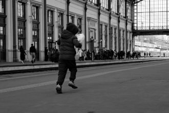Pieni poika juoksee nallen kanssa rautatieasemalla.