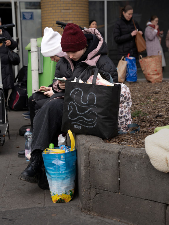 Nuori tyttö istuu aseman edessä syventyneenä puhelimeensa.