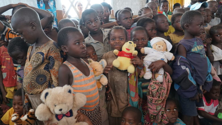 Joukko kongolaisia lapsia hymyilee ja esittelee kameralla pehmolelujaan.