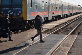 Nainen ylittää junarataa pieni lapsi sylissään