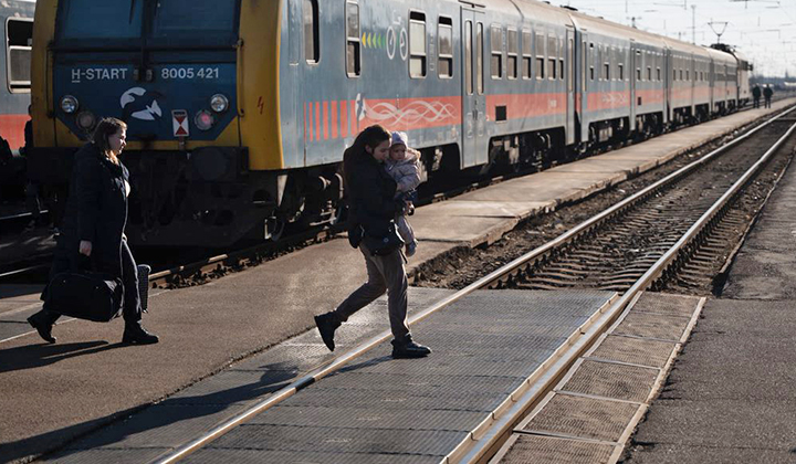 Nainen ylittää junarataa pieni lapsi sylissään