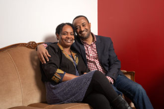 Etiopialainen pariskunta istuu ruskealla sohvalla ja hymyilee.
