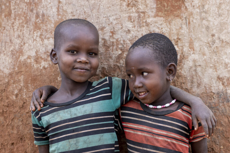 Kaksi ugandalaista lasta vierekkäin raitapaidoissa. Toisella lapsella on käsi toisen olkapäällä.