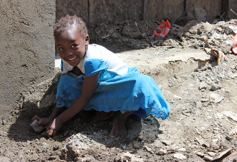 Pieni tyttö sinisessä mekossa leikkii maassa ja hymyilee.