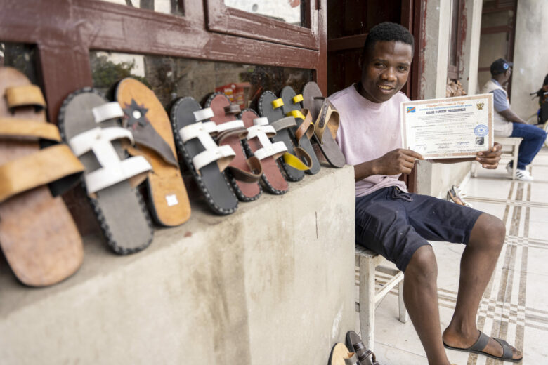 ASAM-järjestön kurssin suorittanut nuori mies esittelee tekemiään sandaaleita sekä kurssitodistustaan.