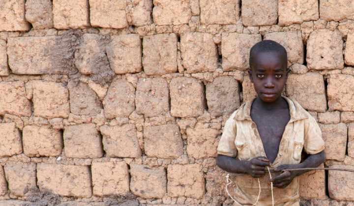 Burundilaislapsi seisoo tiiliseinän edessä