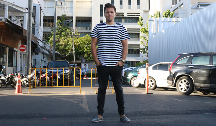 Mies seisoo parkkipaikalla mustissa farkuissa ja raidallisessa t-paidassa.