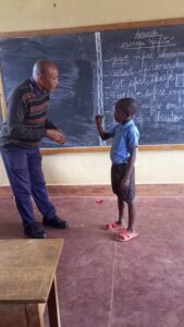 Abayo viittoo opettajansa kanssa luokan edessä.