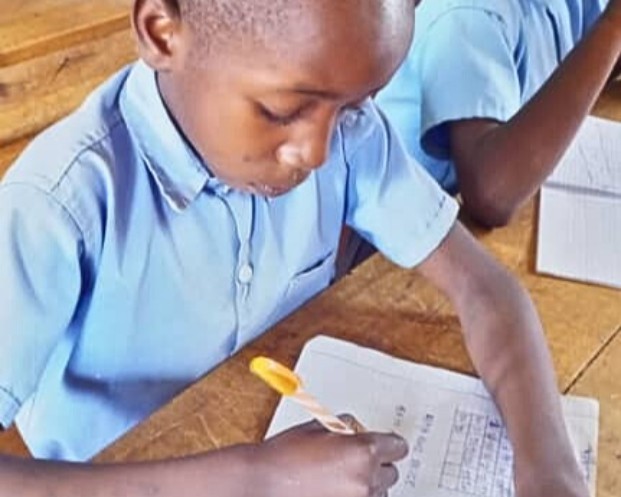 Burundilainen Abayo koulun pulpetissa kirjoittamassa kynällä vihkoon.
