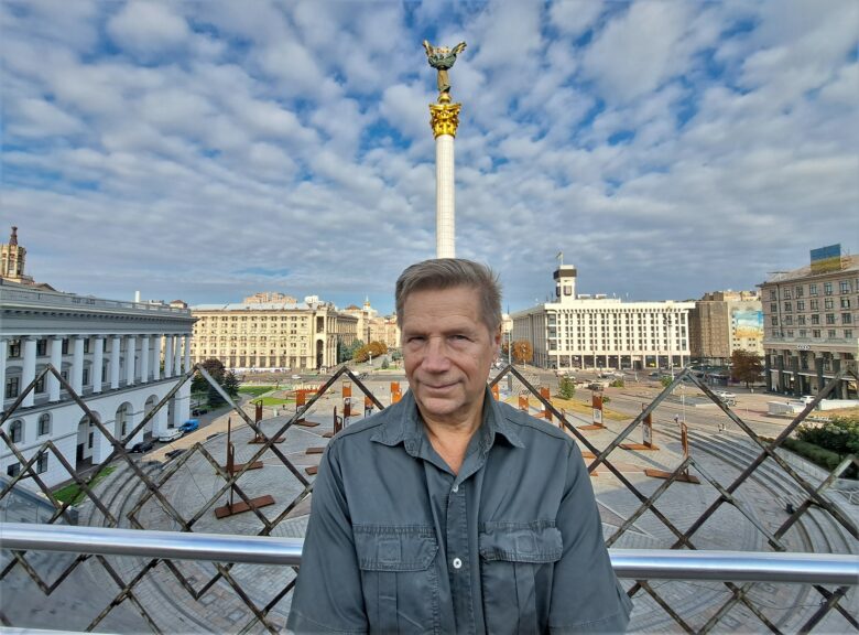 taustalla Kiovan itsenäisyyden aukio ja patsas sen keskellä. etualalla vaalea mies katsoo kameraan.