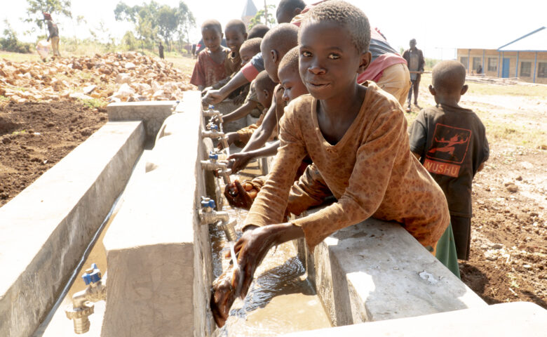Hymyilevä lapsi pesee käsiään koulun pihalla sijaitsevan vesihanan äärellä.