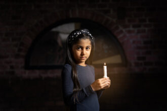 Pitkähiuksinen tyttö, jolla on päässä hiuspanta, pitelee kädessään kynttilää, vasten tummaa taustaa