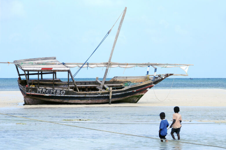 Kaksi lasta ja rannalla oleva puinen vene Tansanian rannikolla.