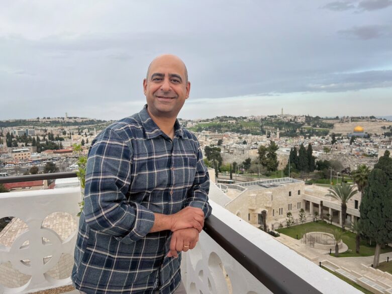 Ruutupaitainen mies seisoo kaiteen edessä. Taustalla näkyy Jerusalem.